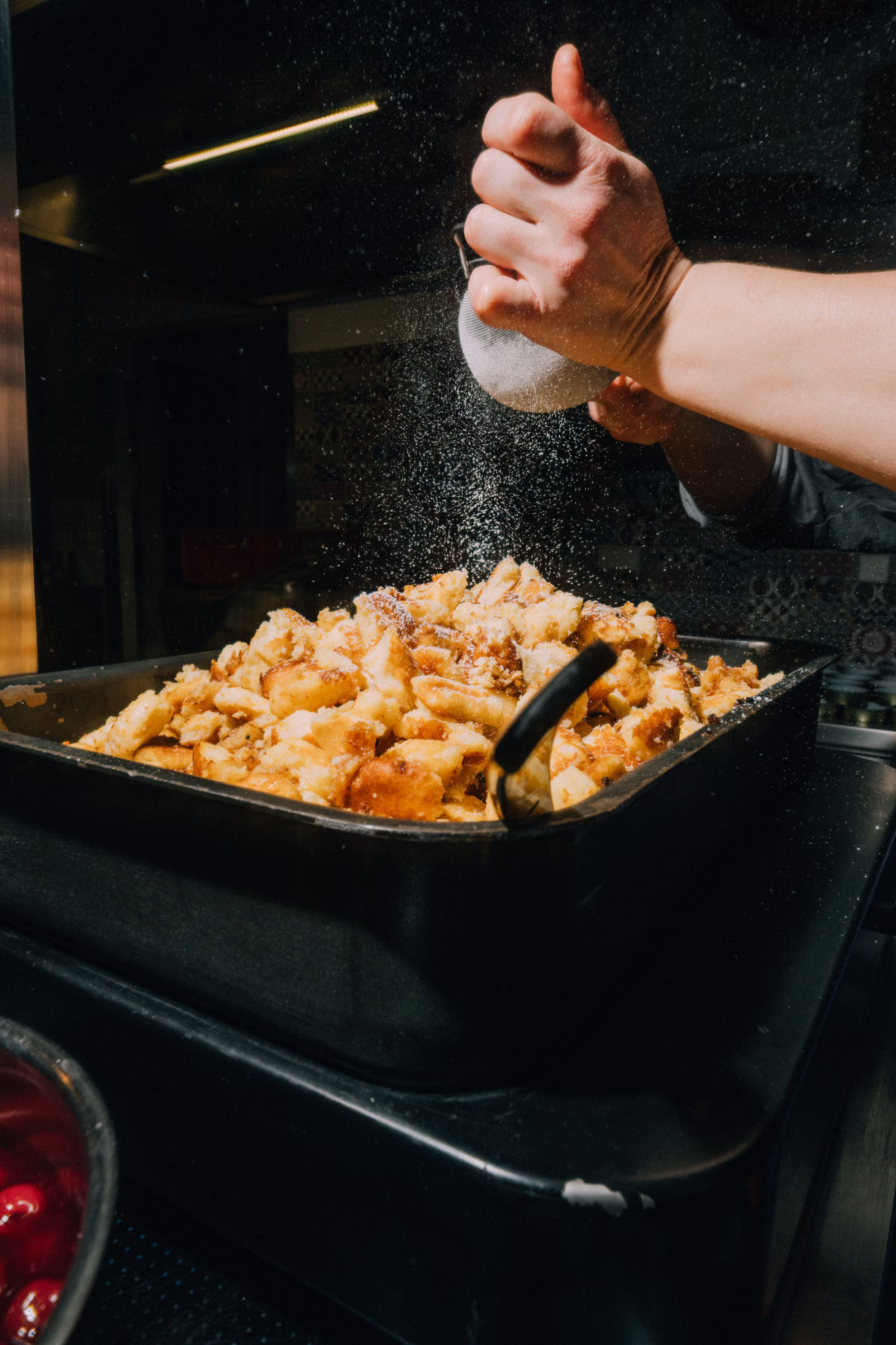Hand bestäubt warme, goldbraune Kaiserschmarrn mit Puderzucker in einer Backform.