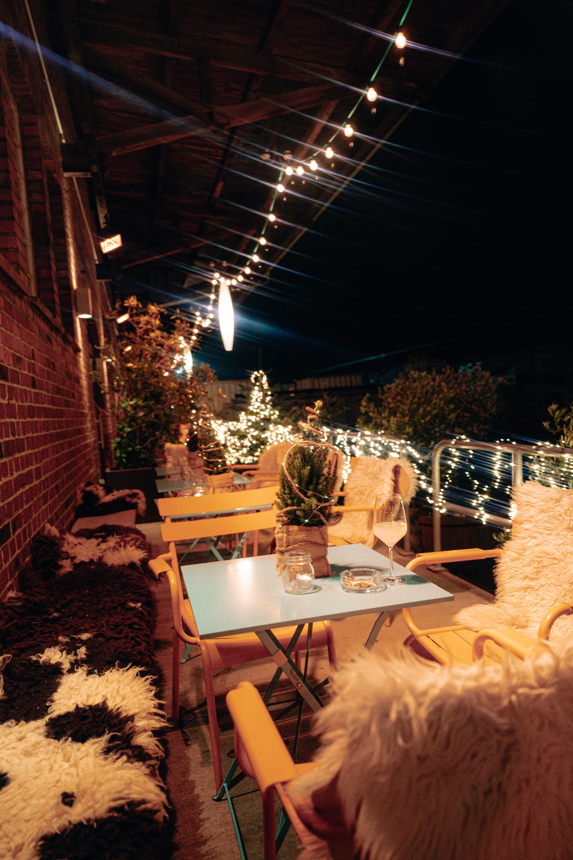 Gemütliche Terrasse mit Tischen, Stühlen und Weihnachtsbeleuchtung bei Nacht.