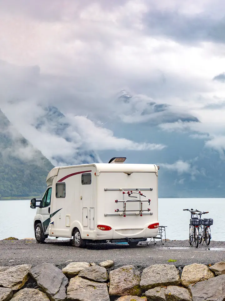 Ein Wohnmobil und zwei Fahrräder, geparkt an einem See, mit nebligen Bergen im Hintergrund.