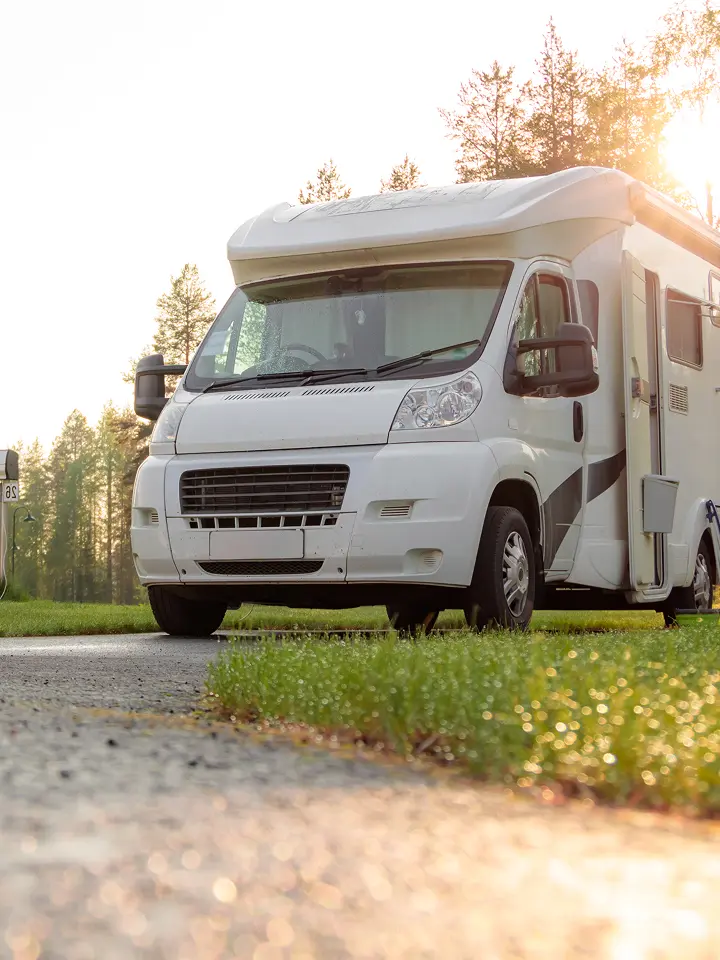 Ein weißes Wohnmobil, das auf einer Wiese geparkt ist, während das Sonnenlicht durch die Bäume im Hintergrund scheint.