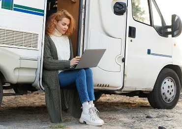 Frau sitzt in der Tür eines Wohnmobils und arbeitet im Freien an einem Laptop.