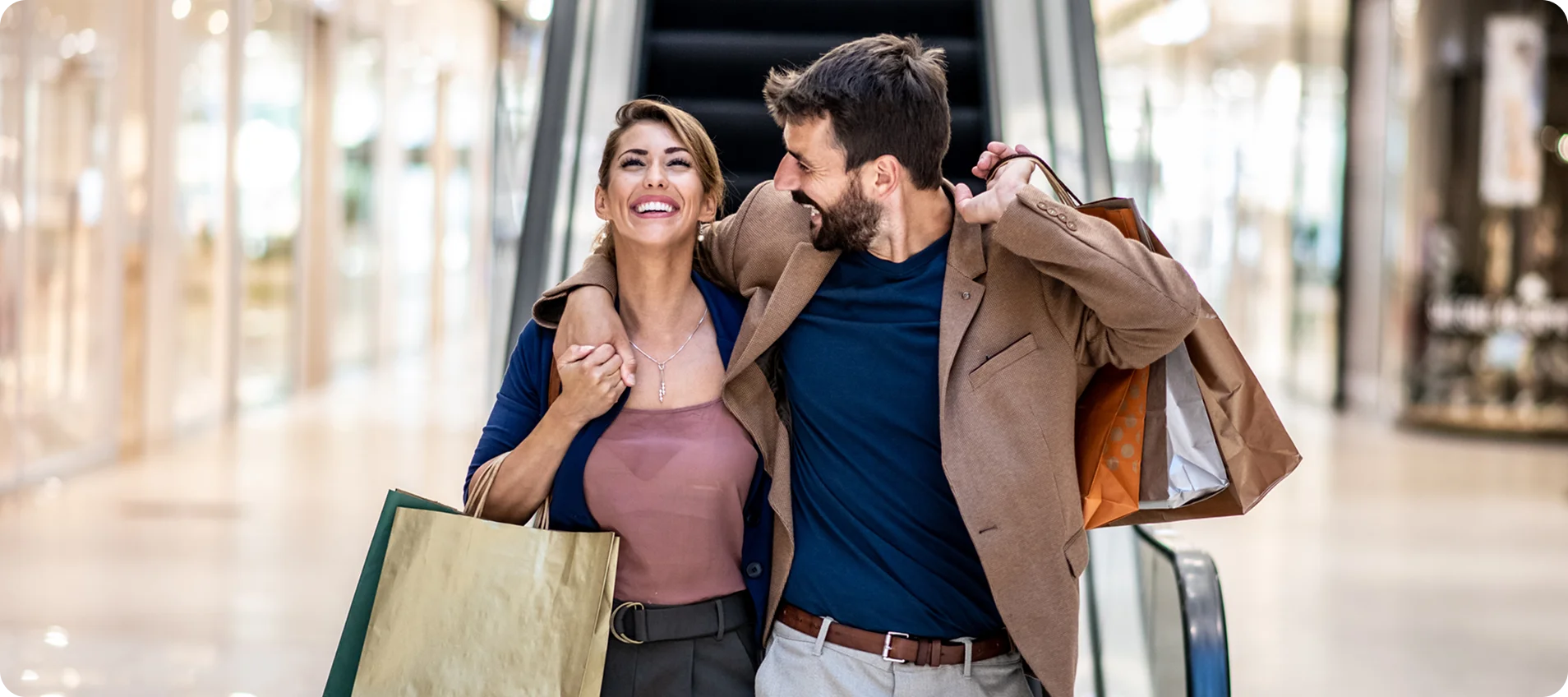 Young attractive happy couple hugging, smiling and holding shopping bags while walking in shopping mall