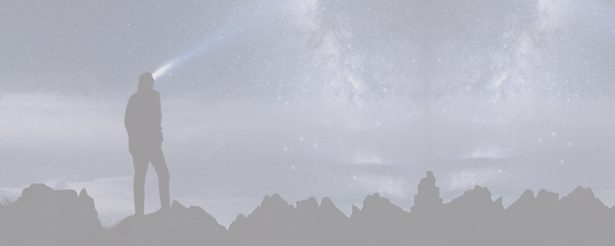 A man standing on top of a mountain under a sky filled with stars.
