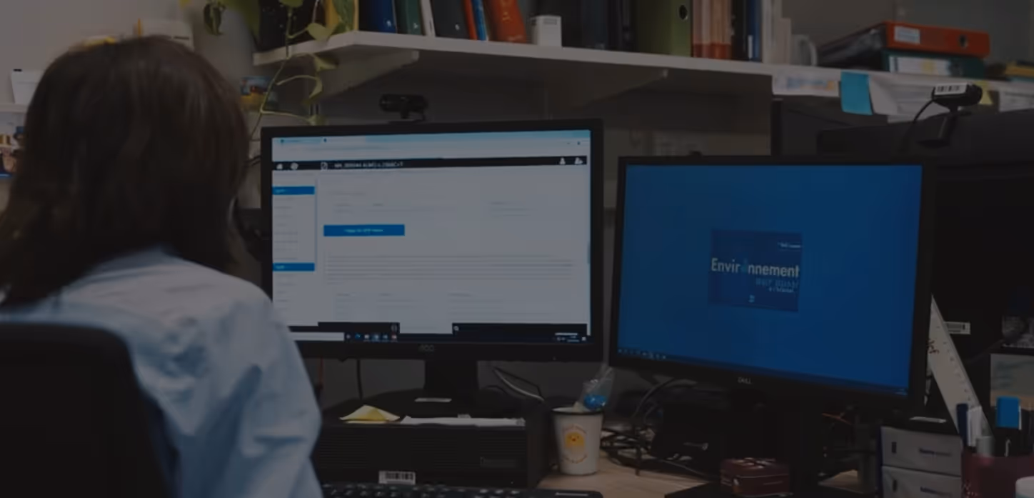 Personne assise devant un bureau avec deux écrans d’ordinateur affichant des pages web et du texte.