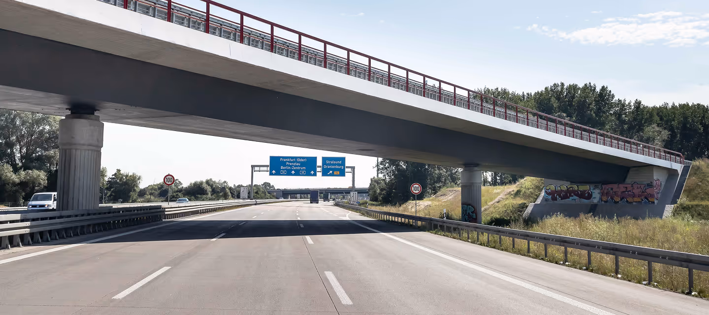 Leere Autobahn unter einer Brücke mit Zielwegweisern nach Frankfurt (Oder), Prenzlau, Berlin-Zentrum und Stralsund Oranienburg, bei Sonnenschein.