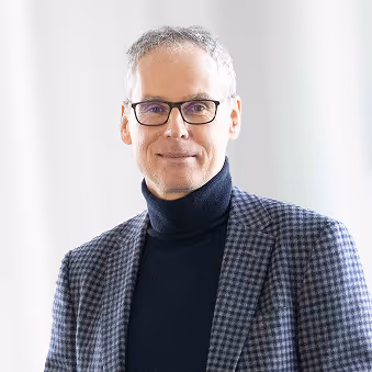 Porträt von Andreas Jancar, Geschäftsführung bei HABAU INFRA, mit Brille, kariertem Blazer und Rollkragenpullover vor hellem Hintergrund