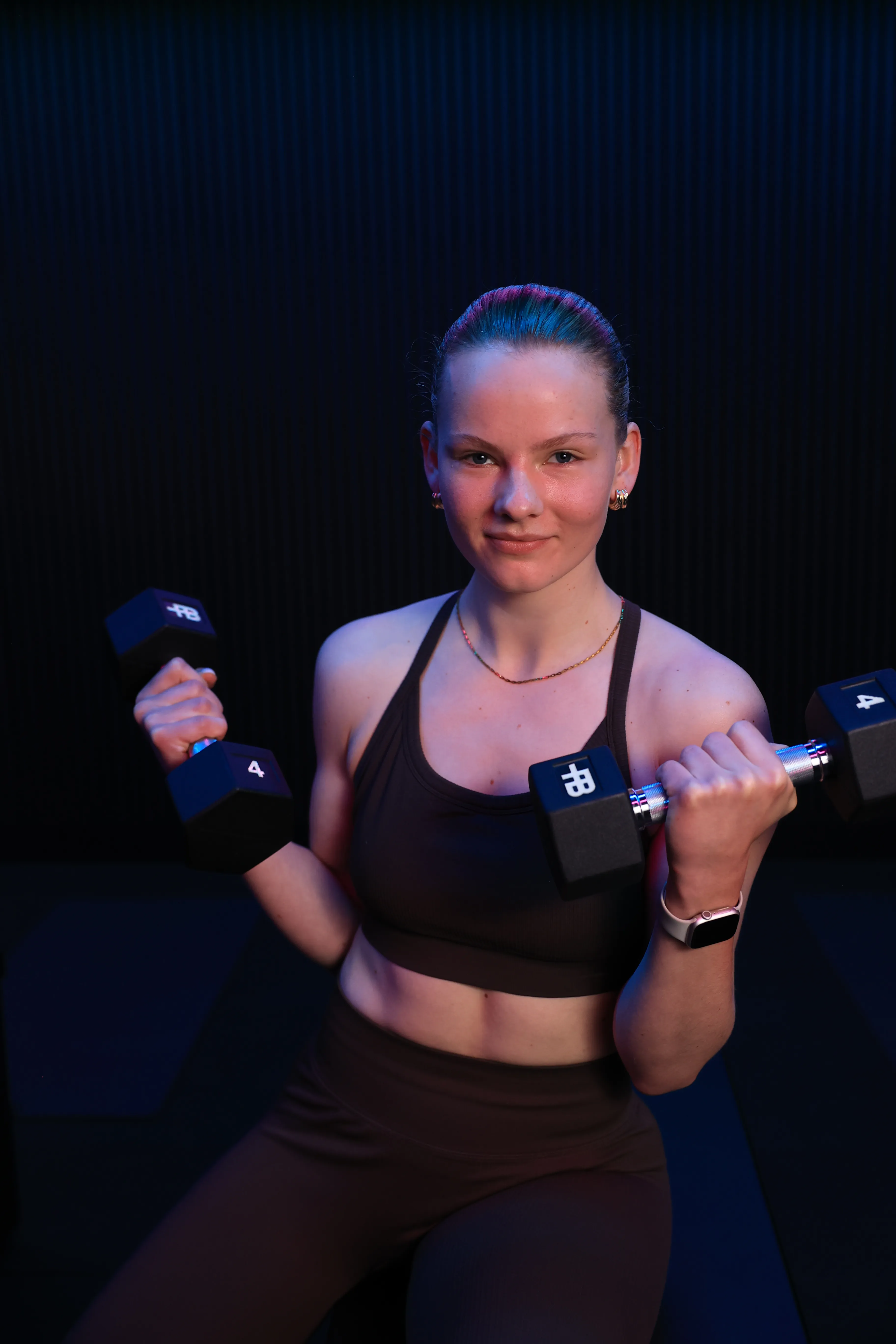 Young woman in black workout attire holding a pair of 4-pound dumbbells in a gym setting.
