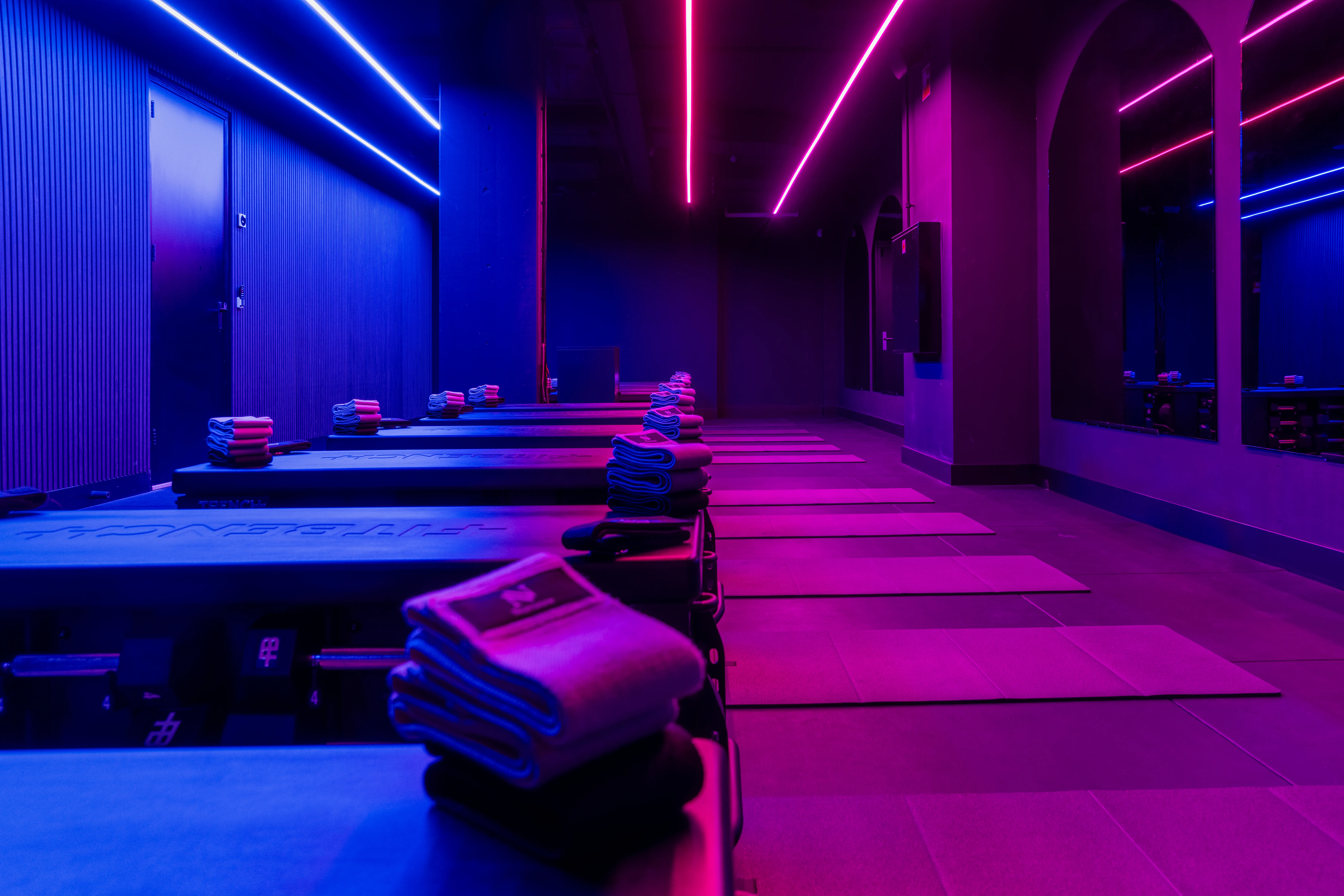 Modern fitness studio with exercise mats and neatly folded towels under blue and purple neon lighting.