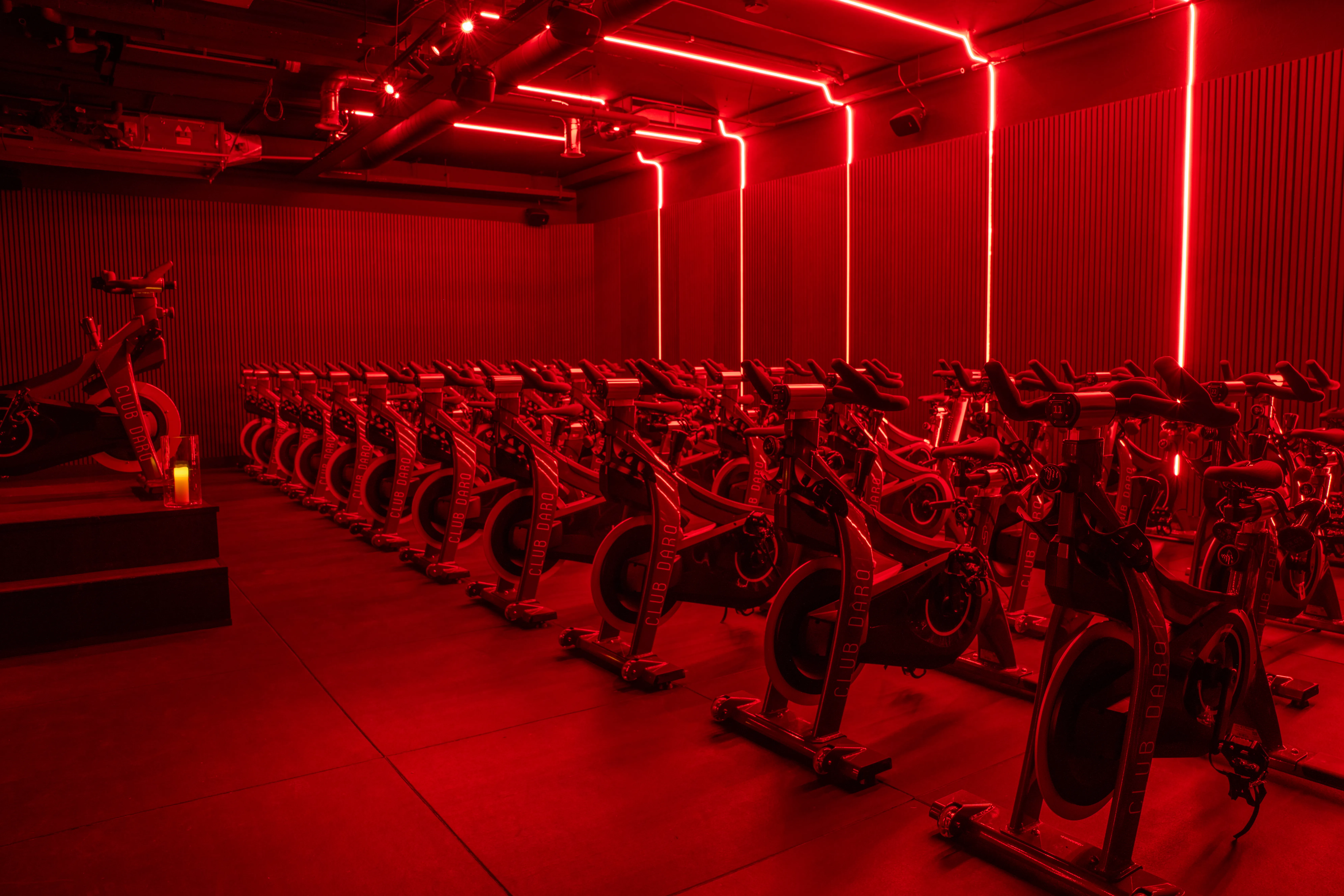Indoor cycling studio with rows of stationary bikes under red neon lighting and modern wall decor.