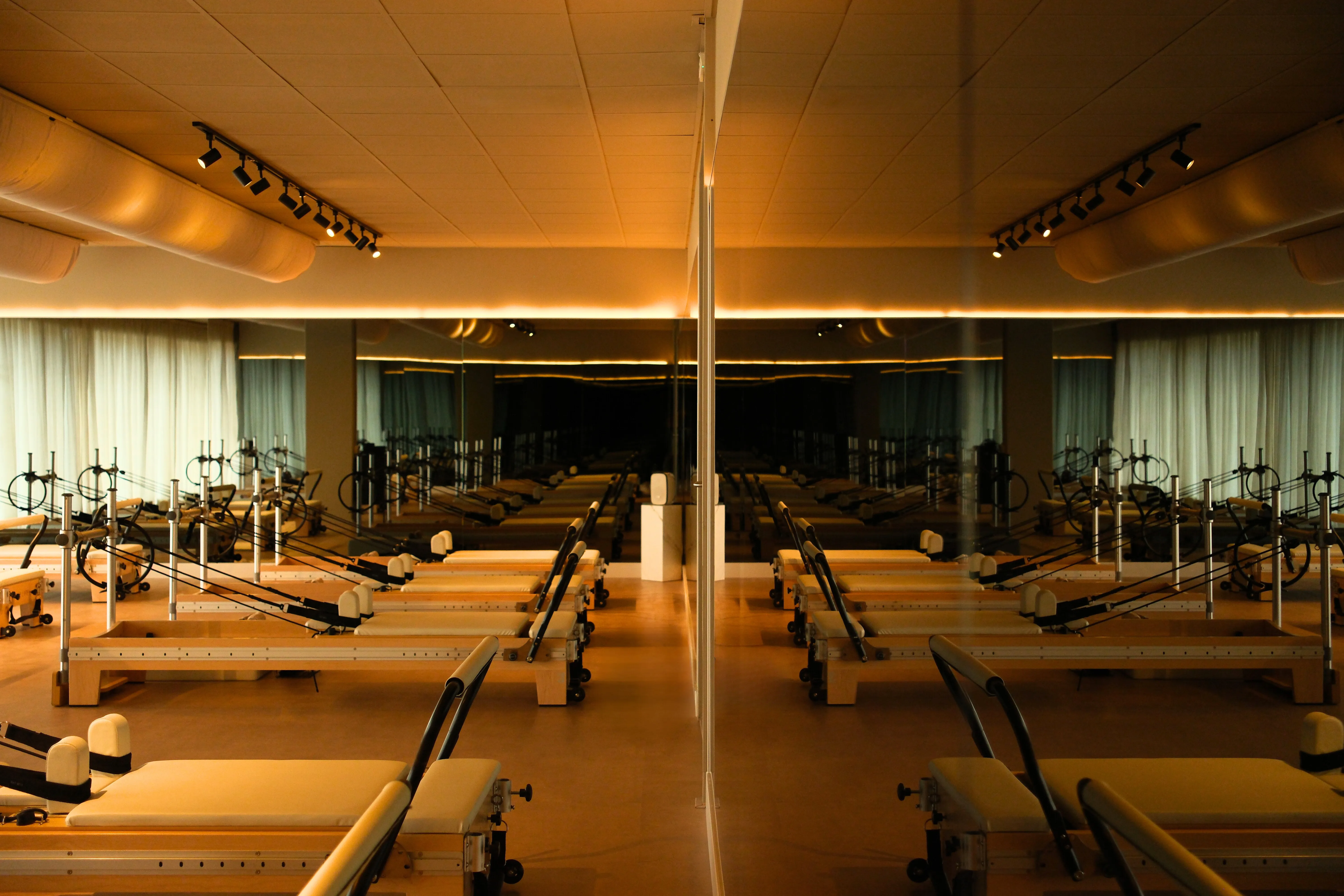 Pilates reformer machines lined up symmetrically in a dimly lit studio with mirrored walls and wooden floors.