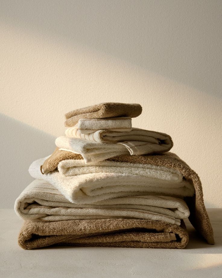 Stack of neatly folded towels in various beige and cream shades on a light surface against a beige wall.