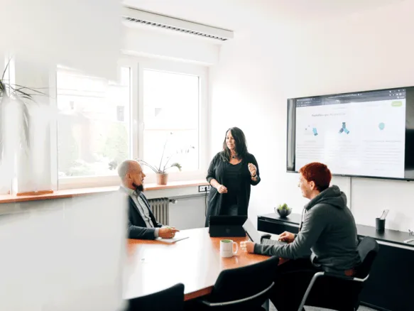 Frau hält eine Präsentation vor zwei weiteren Personen in einem Büroraum