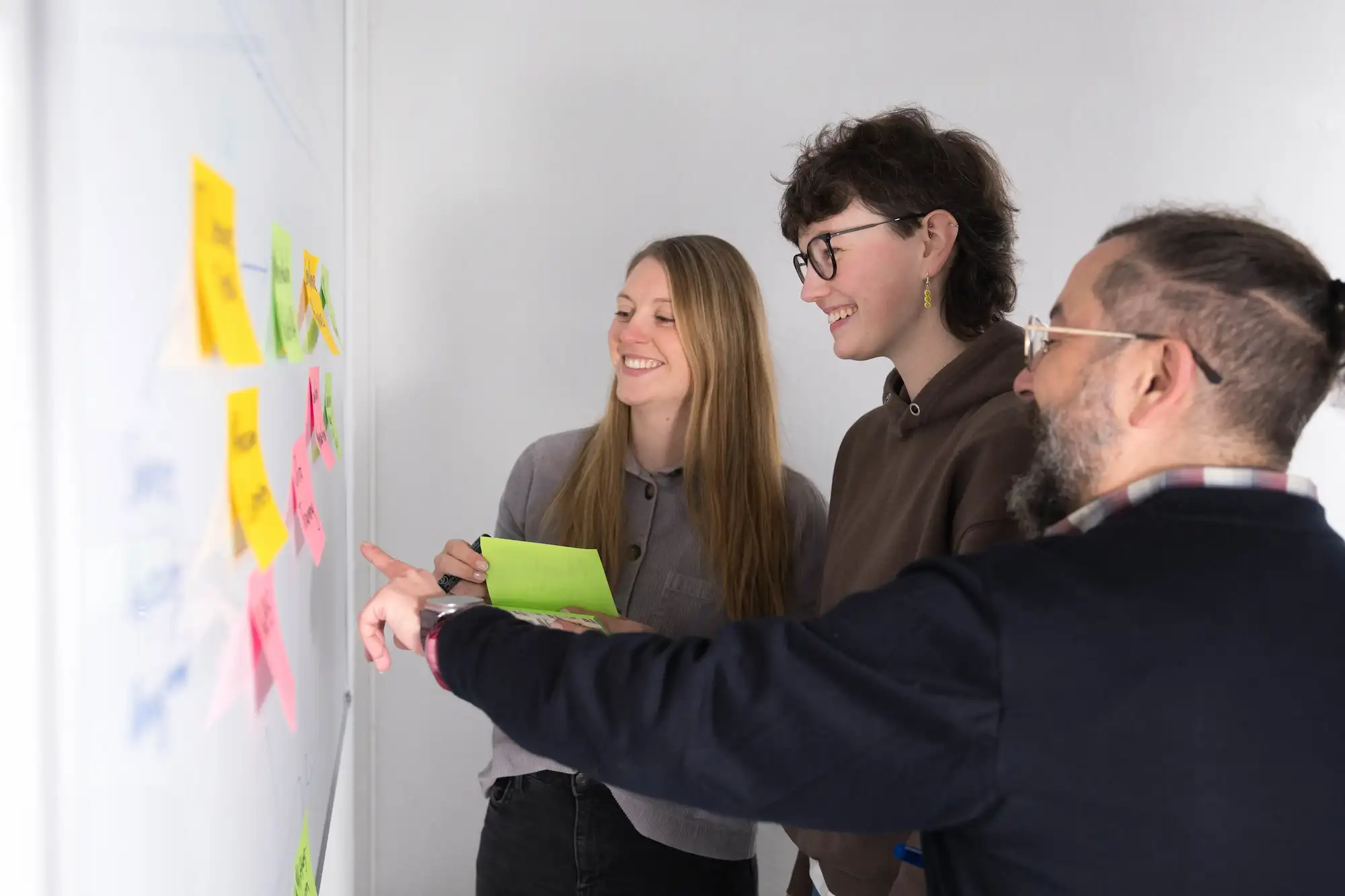 Mehrere Personen stehen vor einem Whiteboard und kleben Post-Its daran.