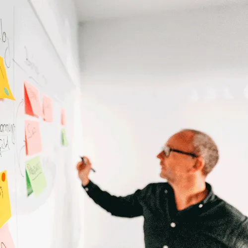 Mann schreibt auf Post-Its auf einem Whiteboard.