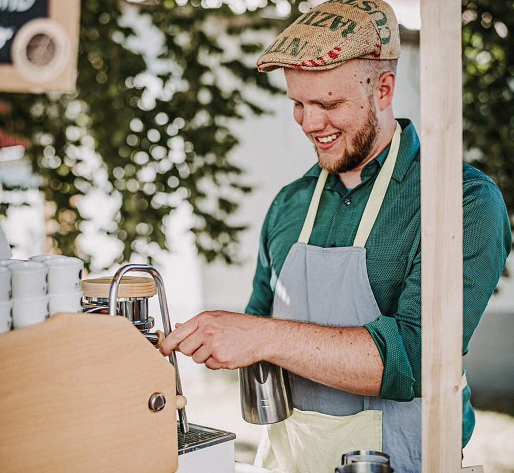Barista steht an einer Espressomaschine und lächelt während der Kaffeezubereitung.