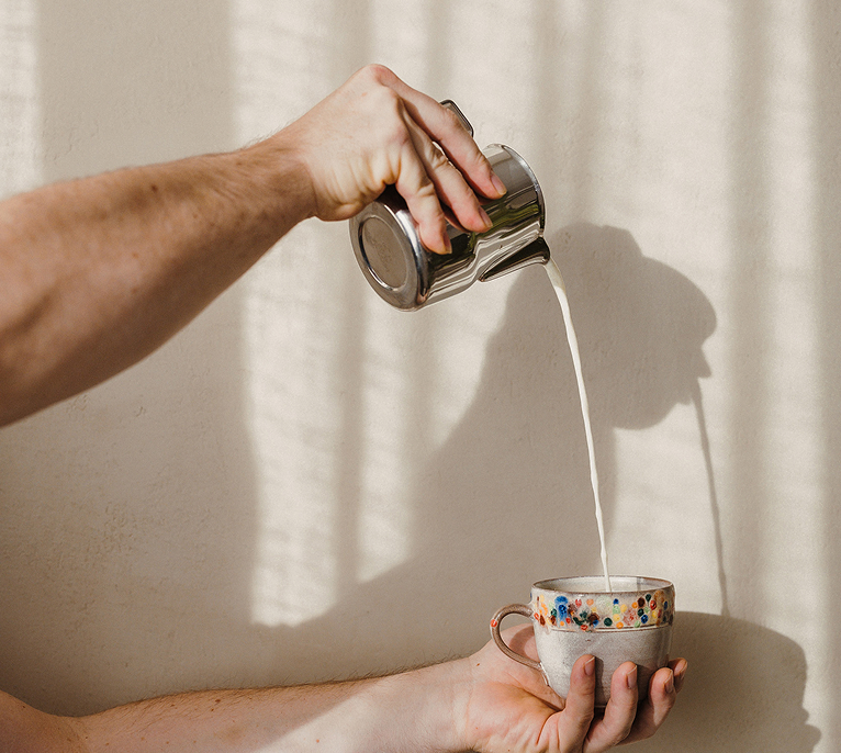 Hand gießt Kaffee aus einer Kanne in eine Tasse