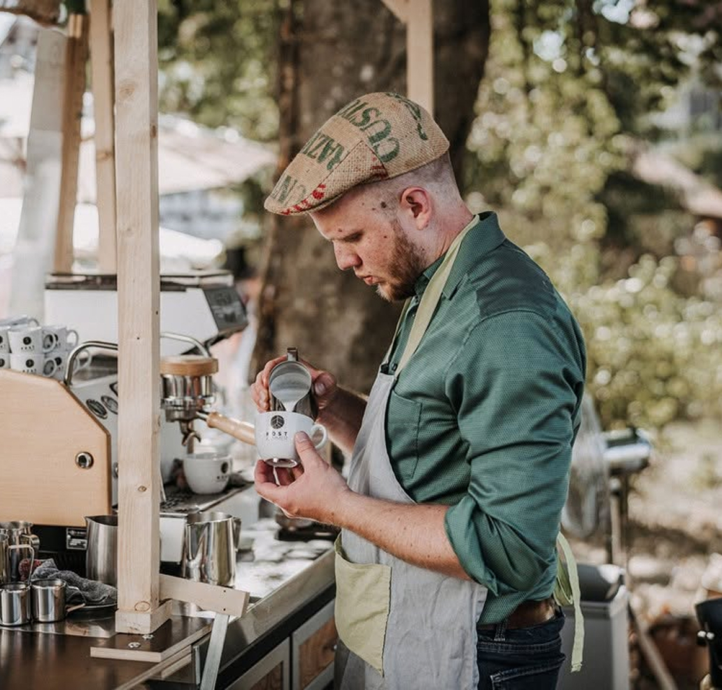 Barista steht an einer Siebträgermaschine im Freien und bereitet Kaffee zu.