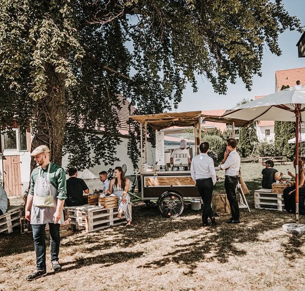 Menschen sitzen und unterhalten sich an einem mobilen Kaffeestand im Freien.