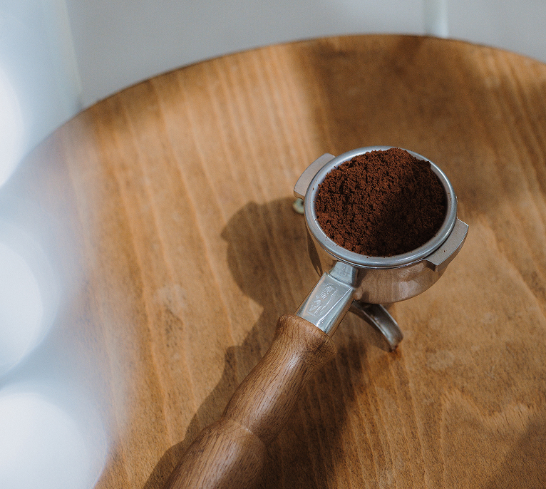 Portafilter with freshly ground coffee resting on a wooden surface.