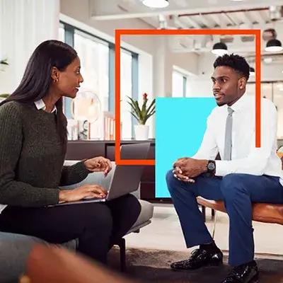 Man and woman sitting indoors with laptop, dressed for work, working together on a project.