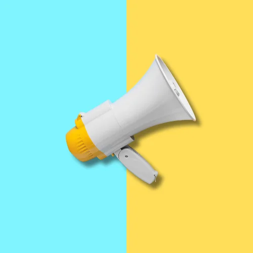 The image features a white and yellow megaphone set against a blue and yellow background. It highlights the design of the loudspeaker, showcasing its bold colors that contrast with the backdrop. The megaphone symbolizes communication and amplification.