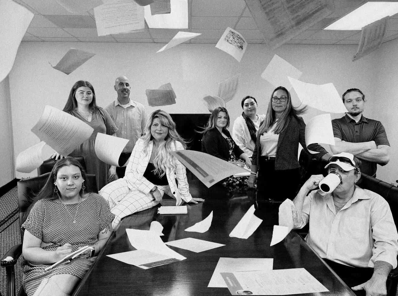 A group of people in a meeting room with resumes flying in the air, some seated, others standing, creating a chaotic yet fun scene.
