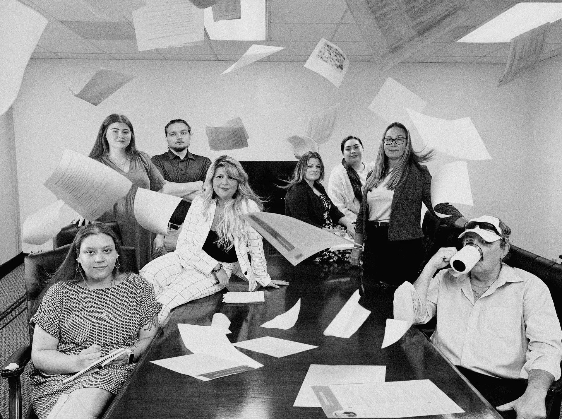 A group of people in a meeting room with resumes flying in the air, some seated, others standing, creating a chaotic yet fun scene.