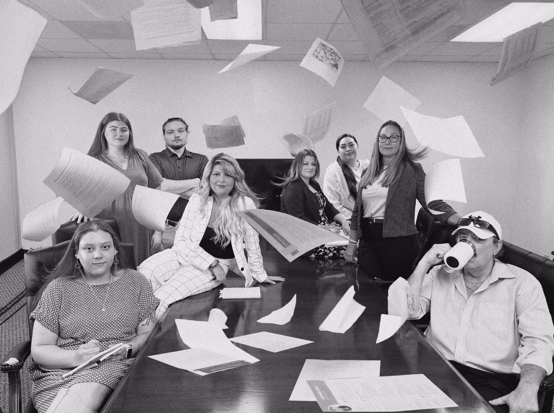 A group of people in a meeting room with resumes flying in the air, some seated, others standing, creating a chaotic yet fun scene.