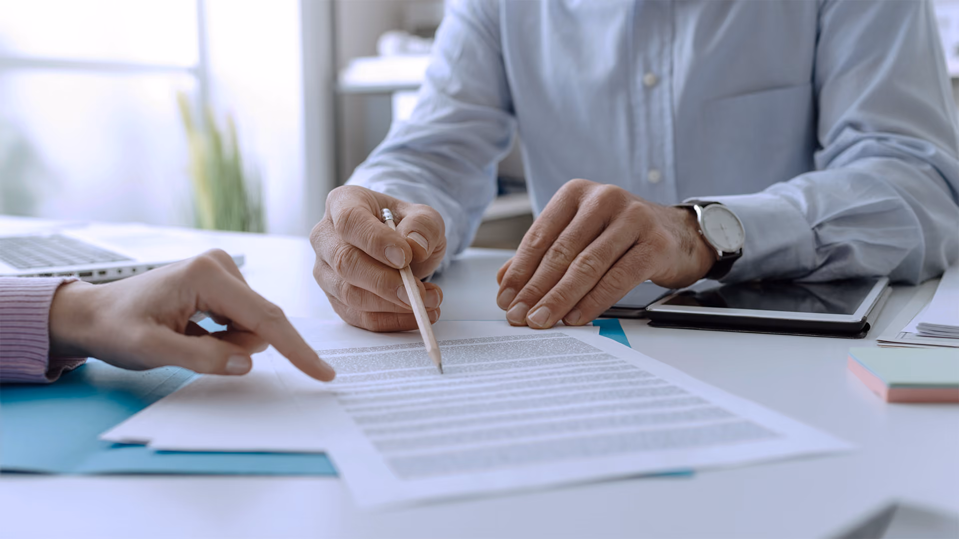 Two people reviewing a document, one pointing and the other holding a pencil ready to sign.