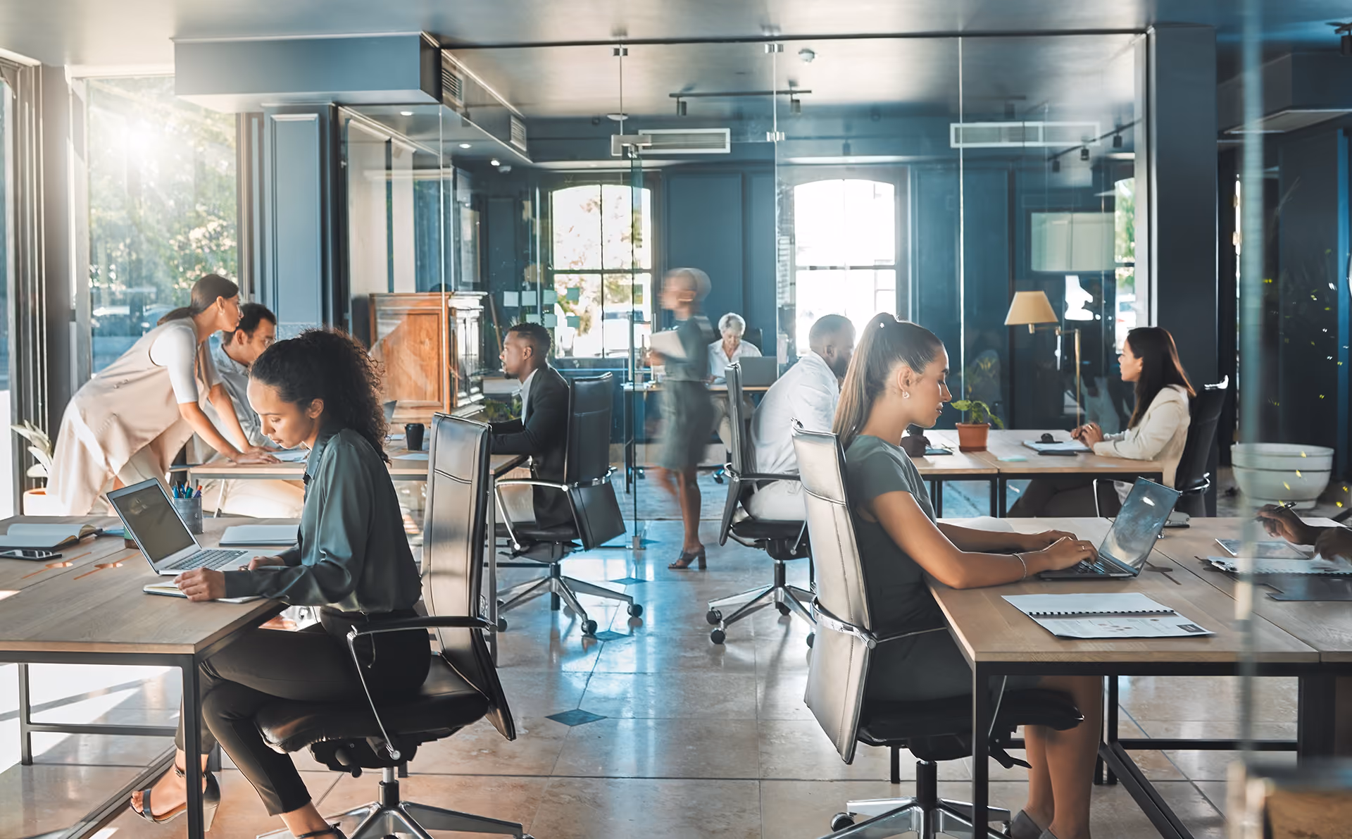Modern open office with diverse professionals seated at desks working on laptops and collaborating.