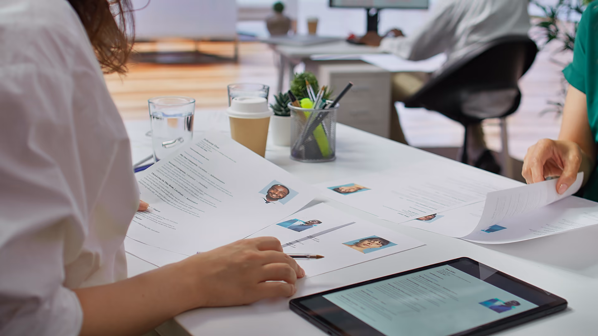 Two people reviewing printed resumes and a tablet with resume details in an office setting.