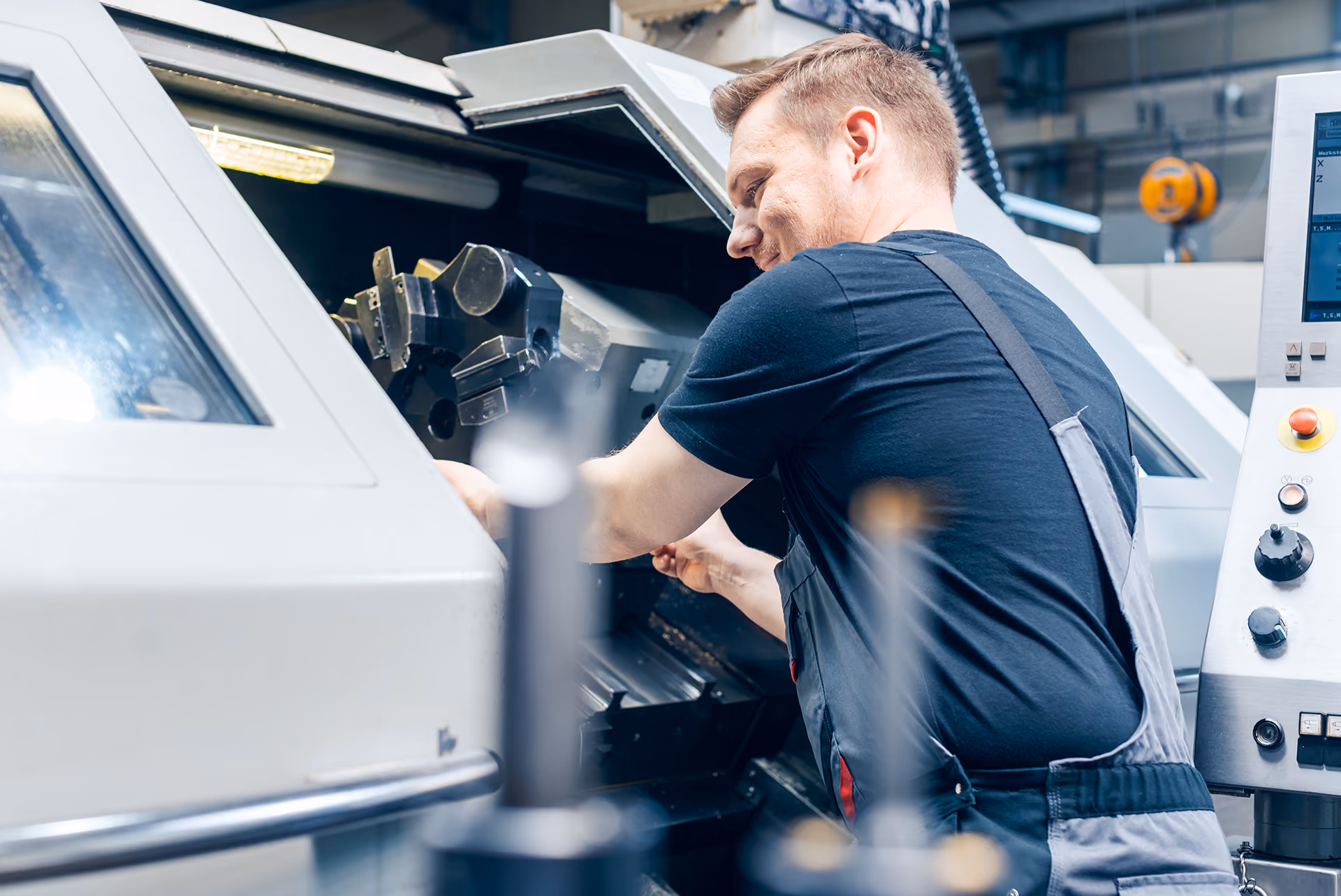 A technician in workwear operates a CNC machine inside an industrial workshop.