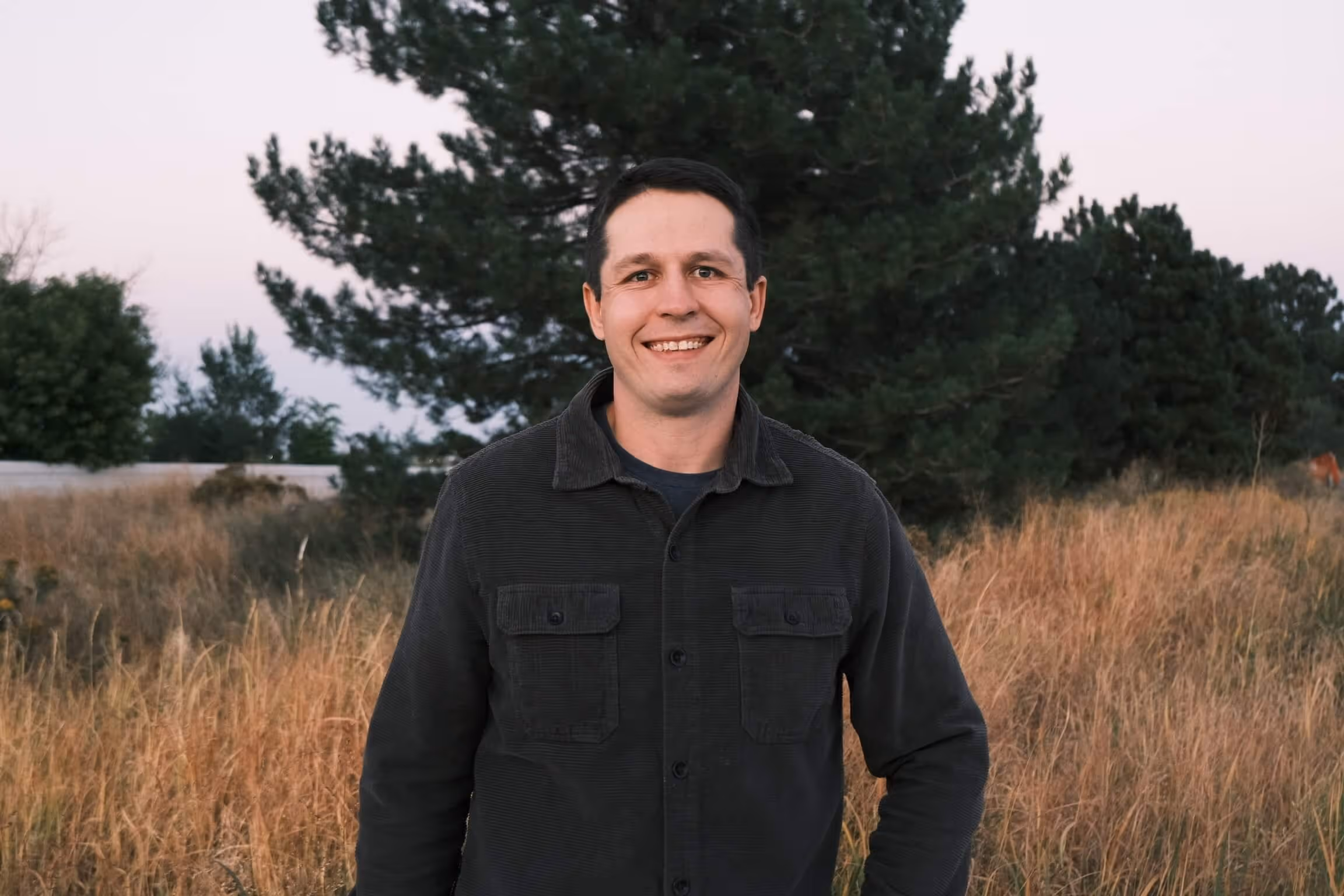 Smiling person standing in golden grass field with trees in background