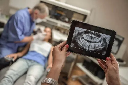 dental staff holdiing up an x-ray image of a patient's teeth while the dentist examine's the patient's mouth