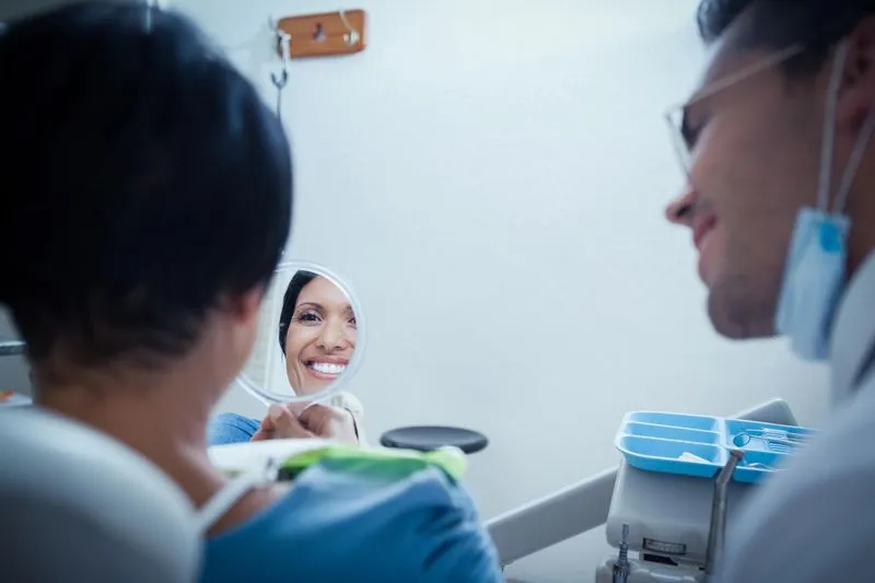 woman at the dentist office looking in the mirror and loving her smile