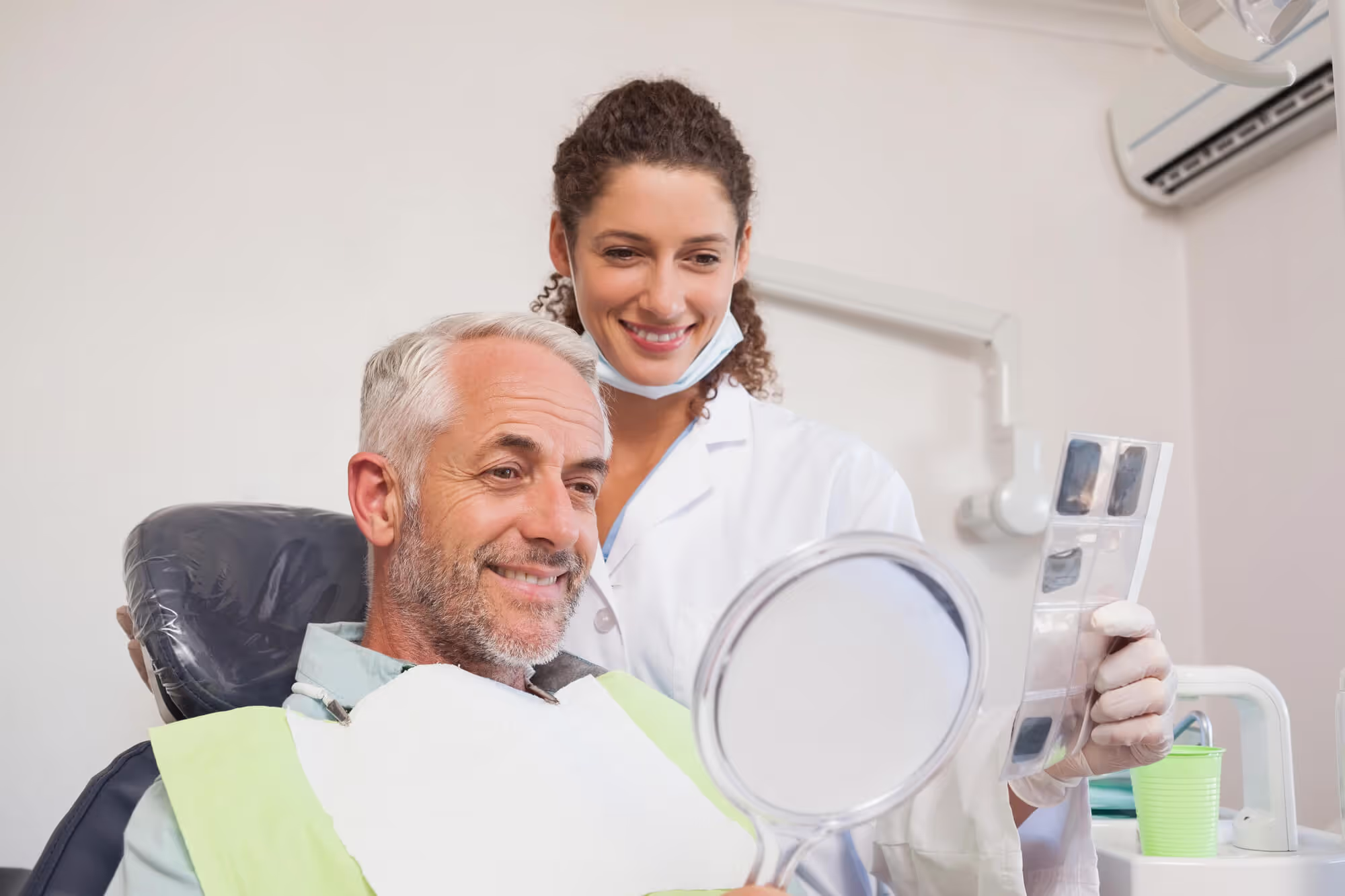 older man at the dentist office looking in the mirror and loving his smile