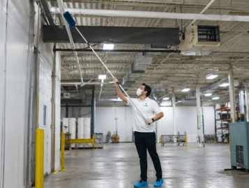CleanWise Solutions industrial cleaning professional performing high ceiling dusting in a warehouse facility.
