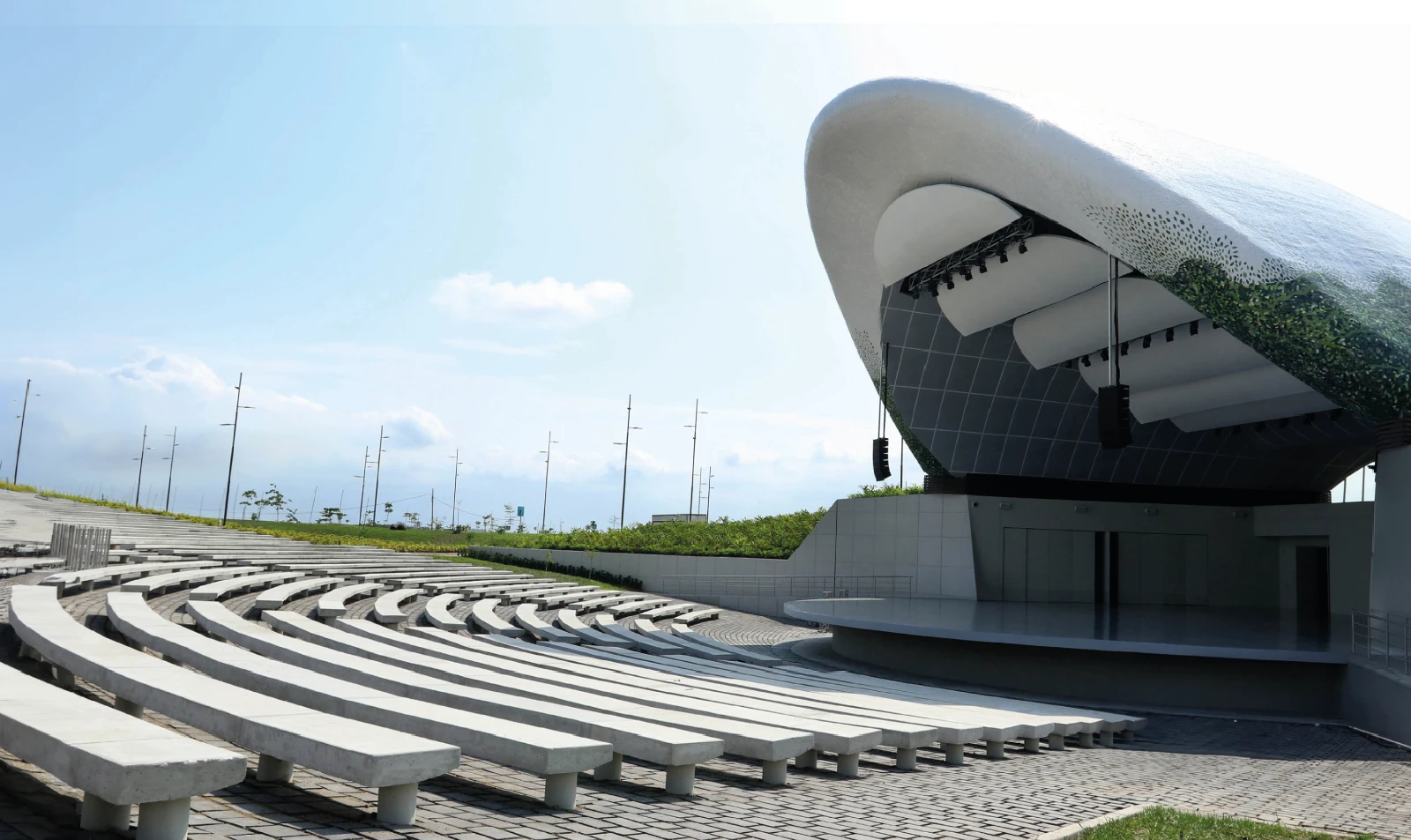 Anfiteatro al aire libre con asientos de concreto en forma de semicírculo y un escenario cubierto con estructura moderna.