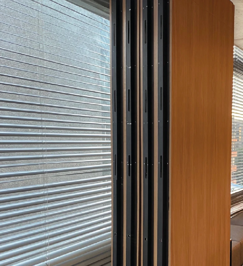 Paneles acústicos móviles de madera alineados junto a una ventana con persianas metálicas.