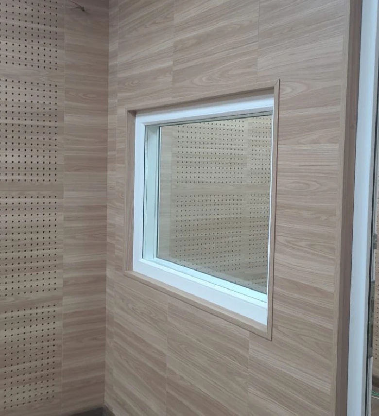 Ventana acústica instalada en una pared con acabado de madera clara y paneles perforados en el interior.
