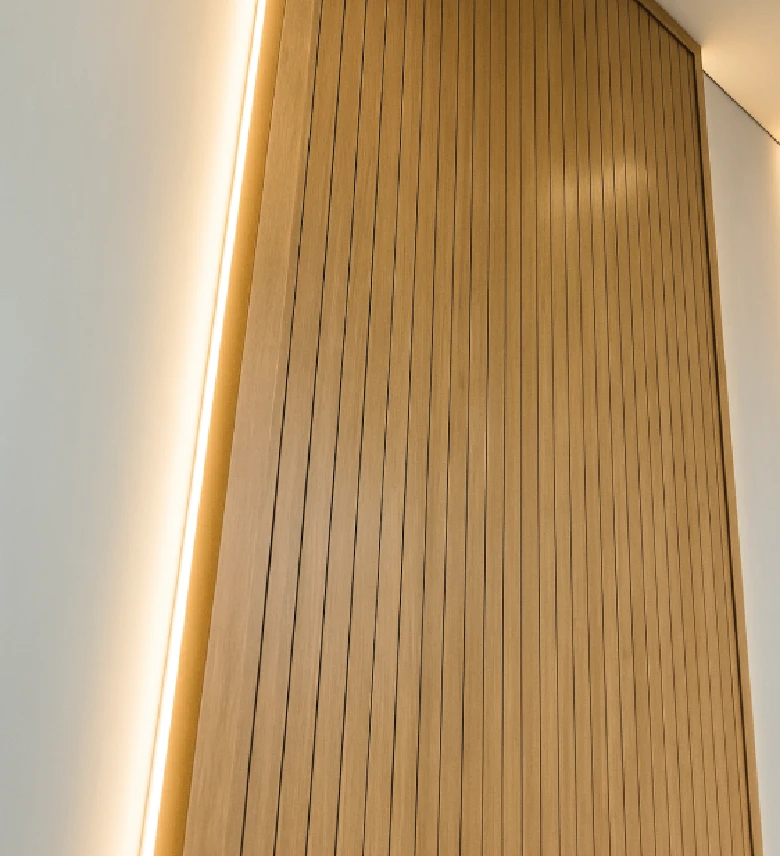 Panel de madera con ranuras verticales instalado en la pared, iluminado con luz cálida en los bordes.
