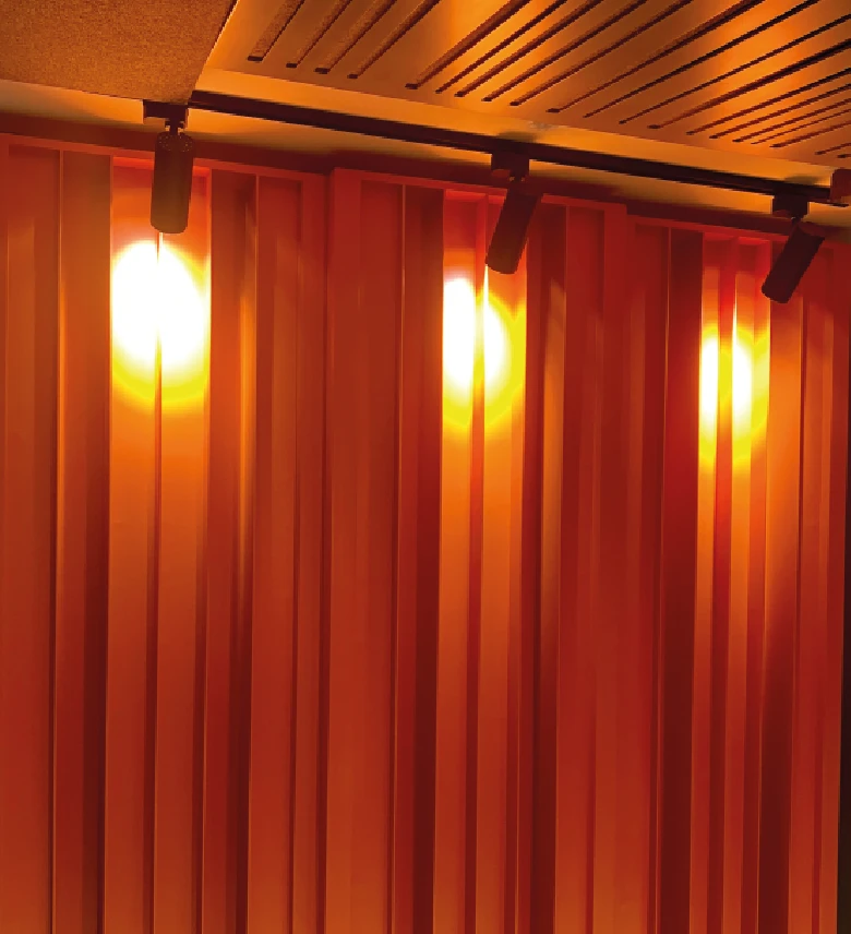 Paneles acústicos verticales de madera iluminados por luces cálidas en el techo de una habitación.