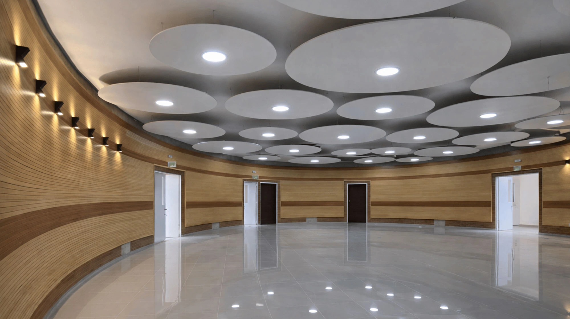 Sala circular espaciosa con paredes de madera y techo con paneles redondos y luces empotradas.