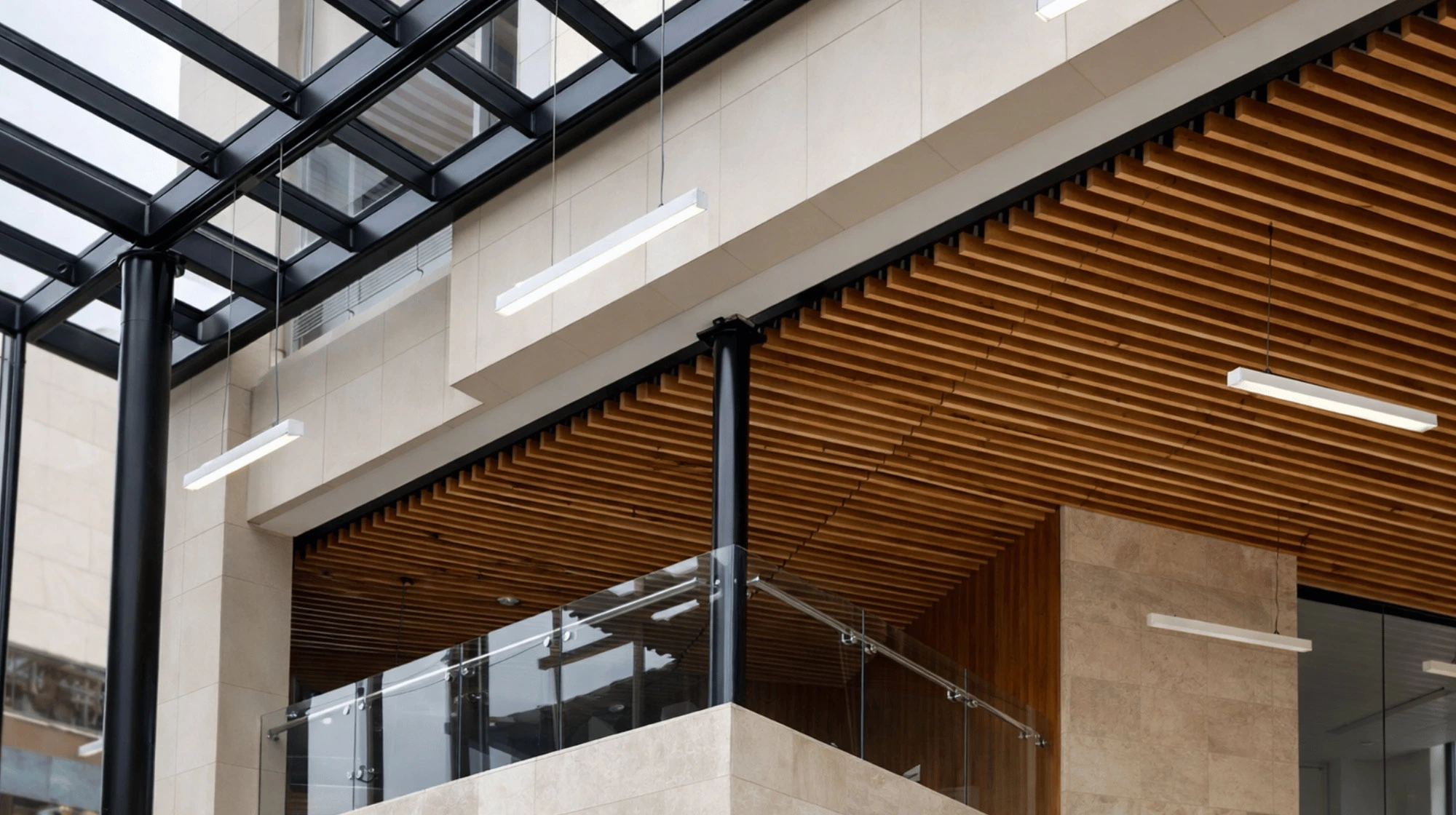 Detalle del interior moderno con techo de listones de madera, columnas negras, paredes claras y barandales de vidrio.