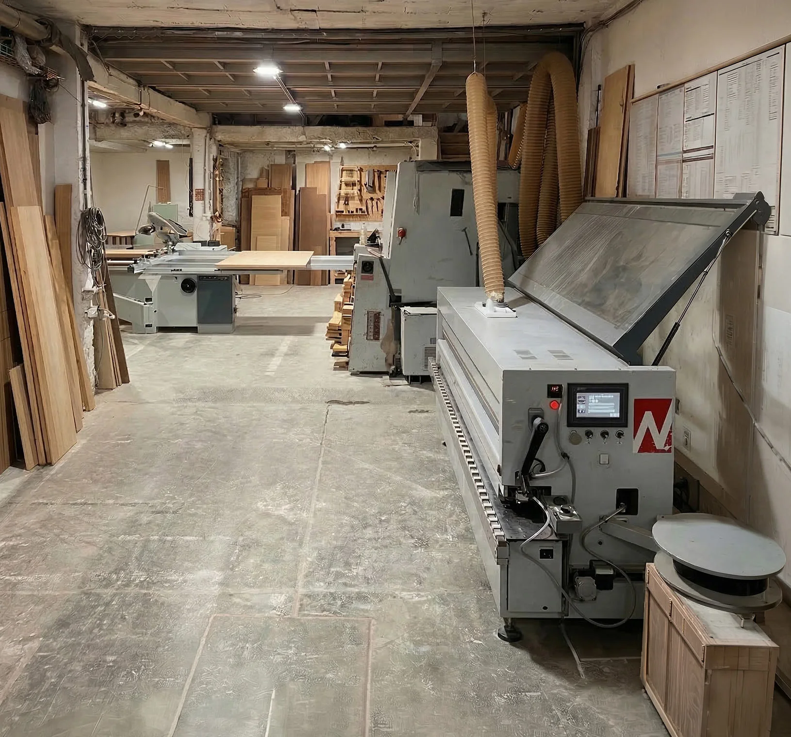 Interior de un taller de carpintería con maquinaria industrial y tablas de madera apiladas.