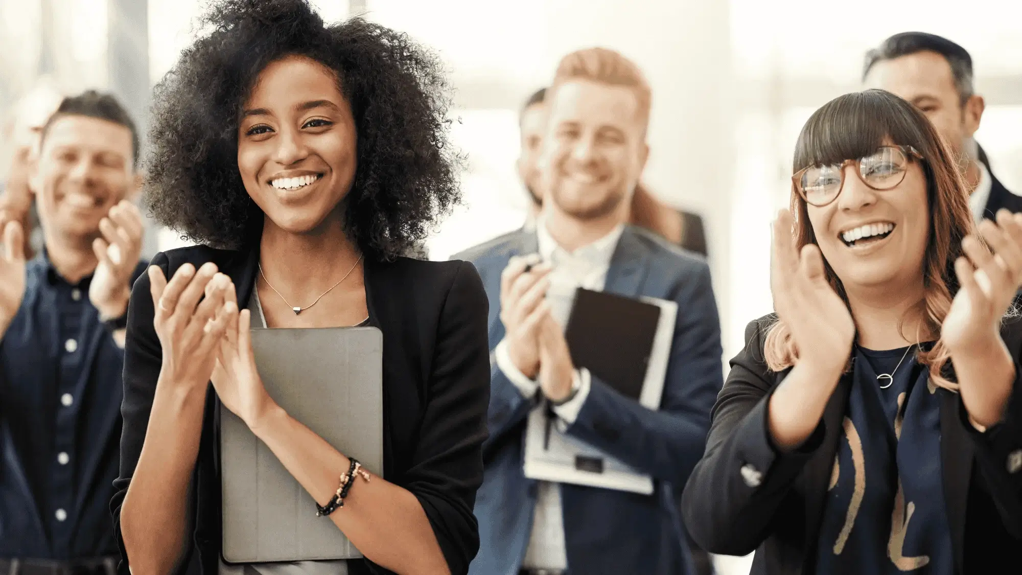Diverse group of professionals applauding and smiling in a workplace setting, representing employee engagement, positive company culture, and successful long-term retention.