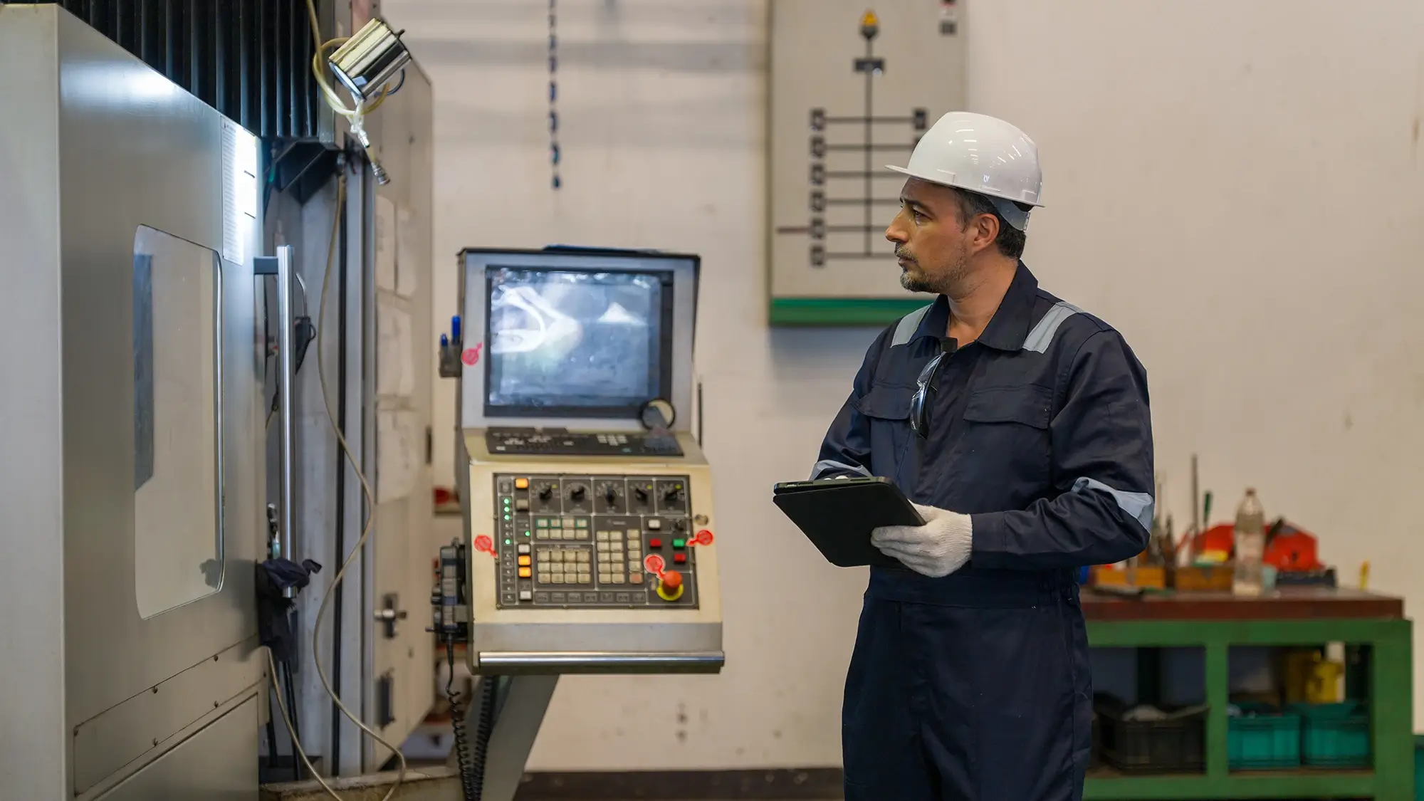 A manufacturing technician troubleshooting a CNC machine with a tablet on a modern factory floor.