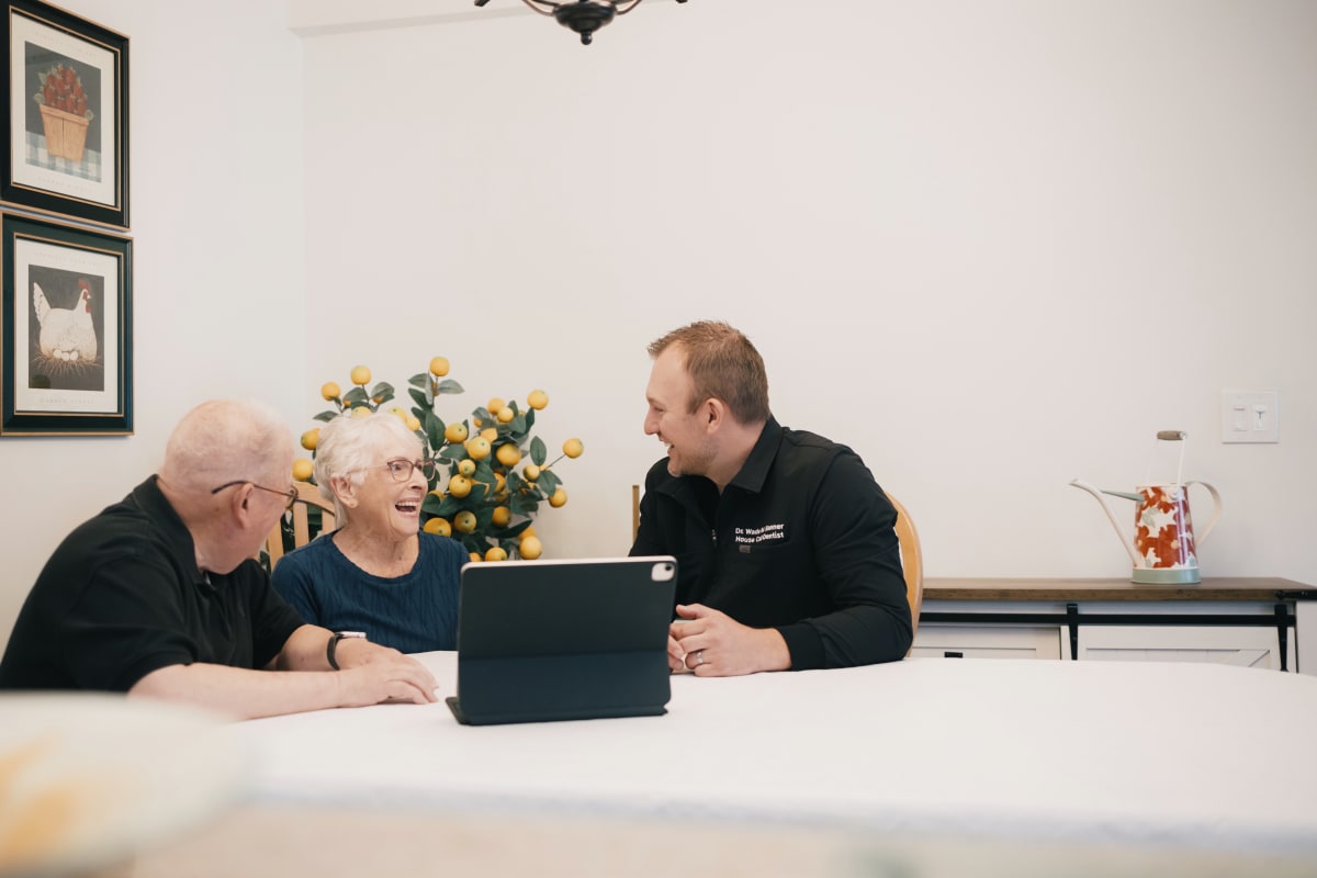 Dentist and elderly patient reviewing dental information on tablet during home consultation