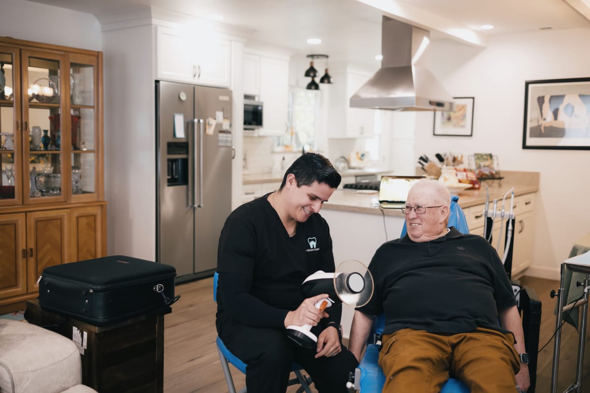 Dentist in black shirt examining senior patient in dental chair at home