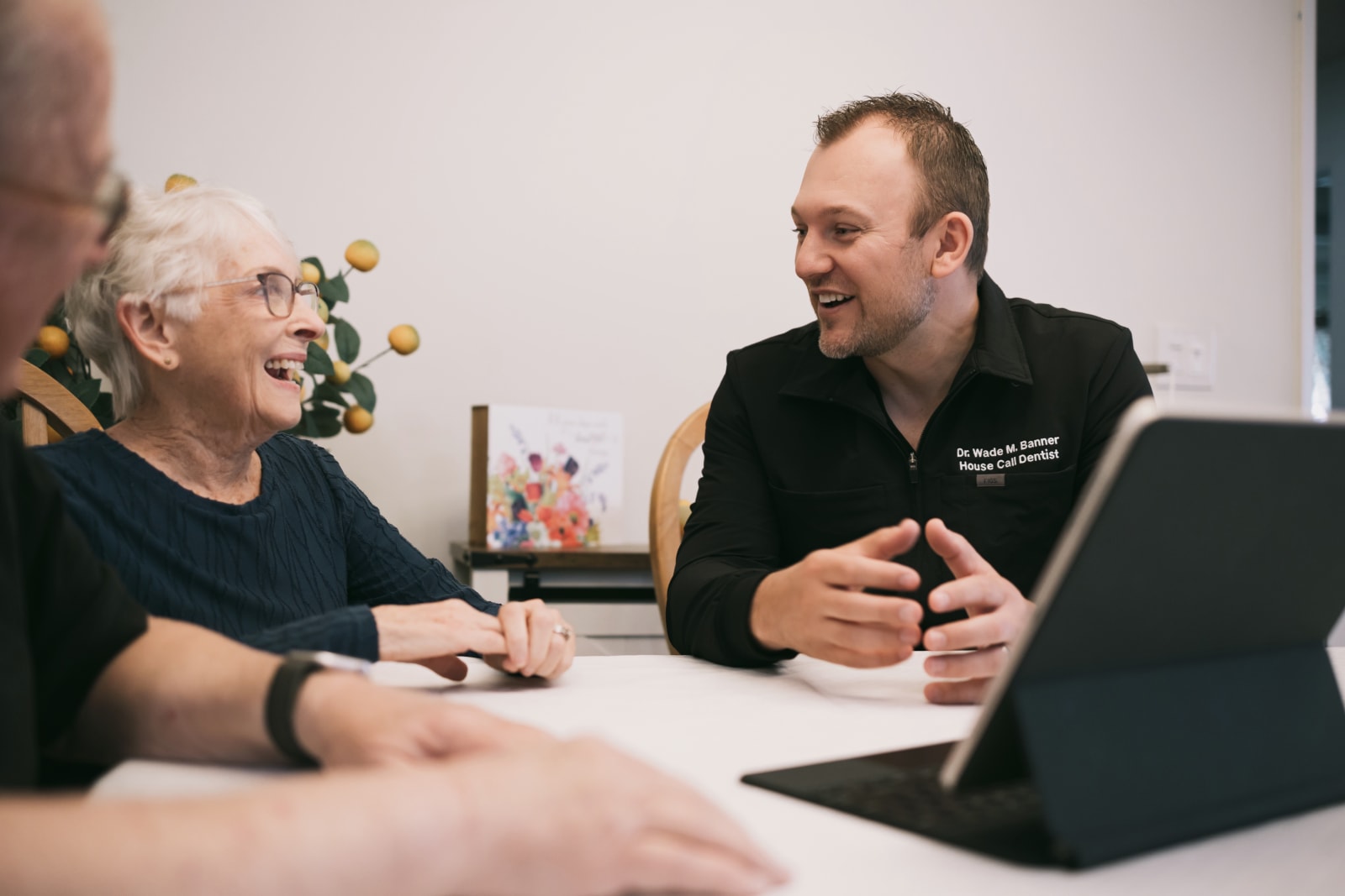 Dentist consulting with an older patient at a table with a laptop